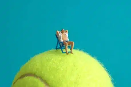 homem tomando sol em cima de bola de tenis