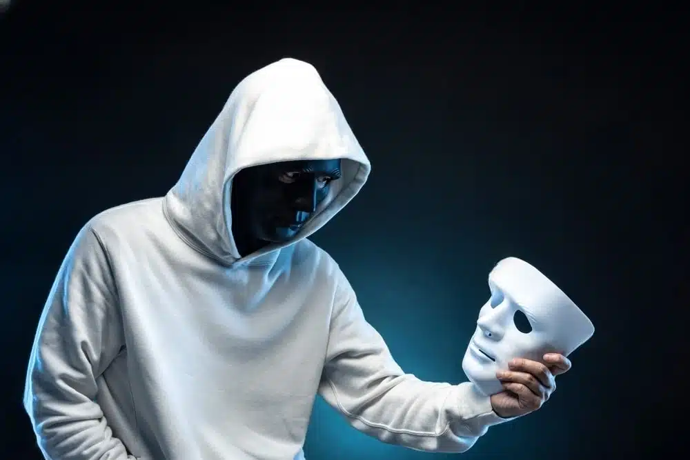 Homem mascarado, com mascara em negro, com máscara em branco na mão, ao estilo Shakespeare, ser ou não ser, representando uma possível psicopatia