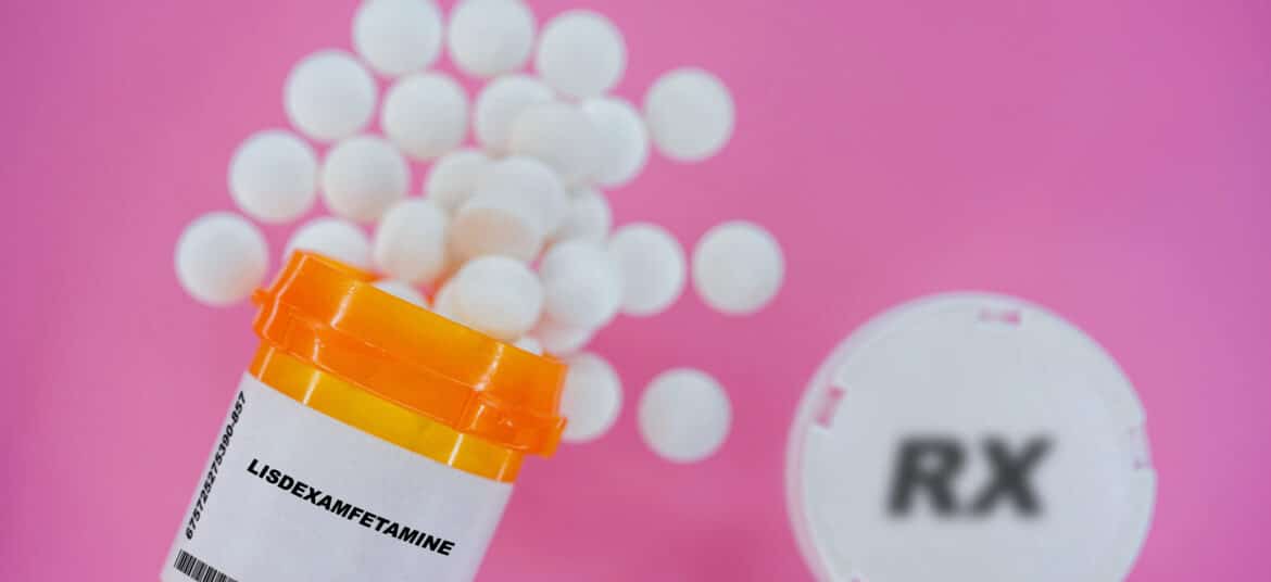 Comprimidos de medicamento prescrito Lisdexamfetamina em um frasco de plástico com comprimidos. Pílulas derramando de um recipiente amarelo sobre um fundo rosa.