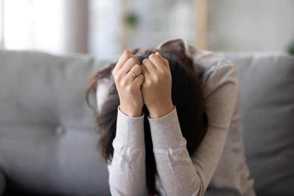 mulher sentada no sofá debruçada com as mãos na cabeça, ela tem sintomas de CID F41