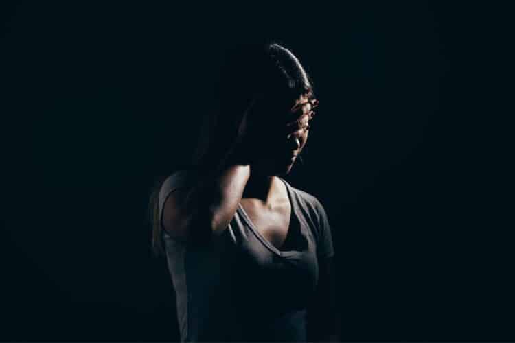 mulher com as mãos na cabeça sinalizando preocupação em um ambiente escuro