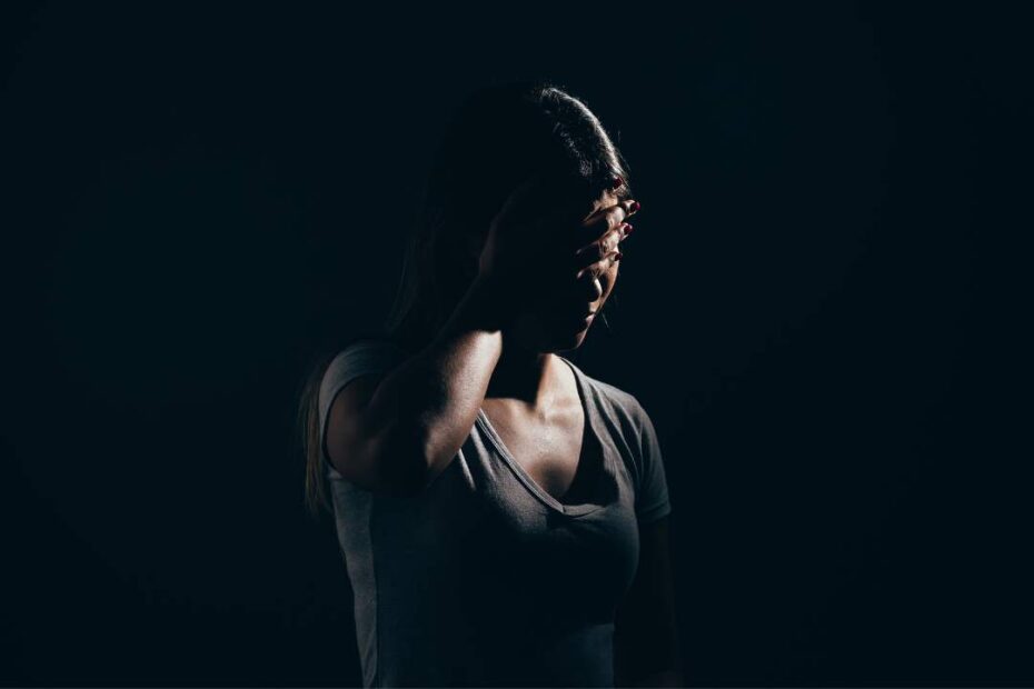 mulher com as mãos na cabeça sinalizando preocupação em um ambiente escuro