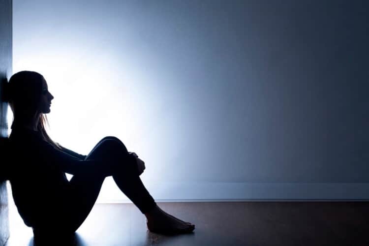 mulher sentada no chão de uma sala, com sintomas depressivos