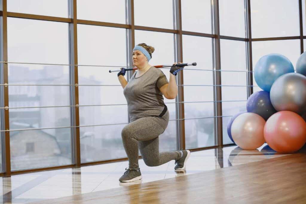 uma mulher está na academia segurando uma barra sobre o ombro, ela está fazendo exercícios