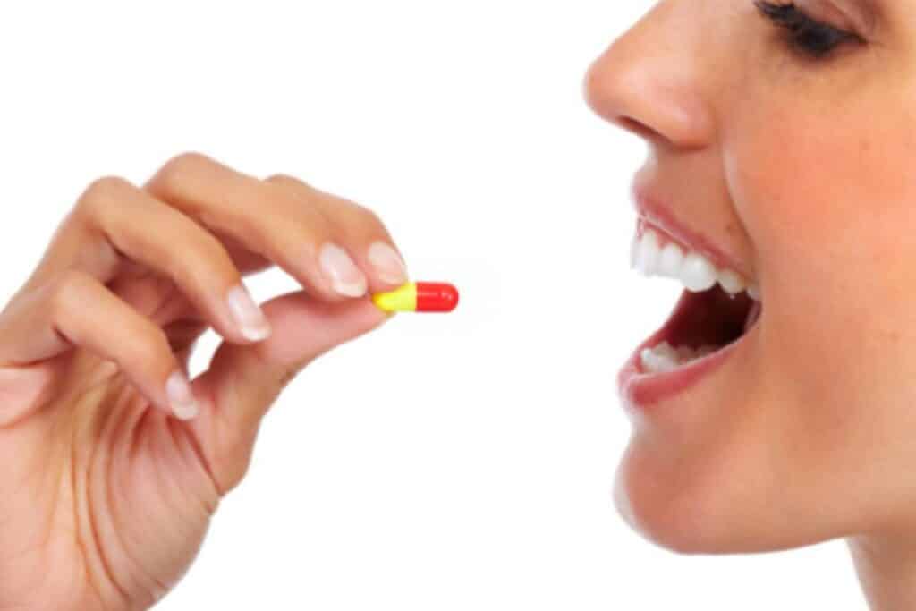 mulher ingerindo um comprimido colorido