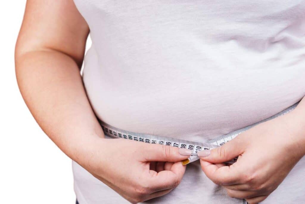 uma pessoa com sobrepeso medindo a própria barriga com uma fita métrica