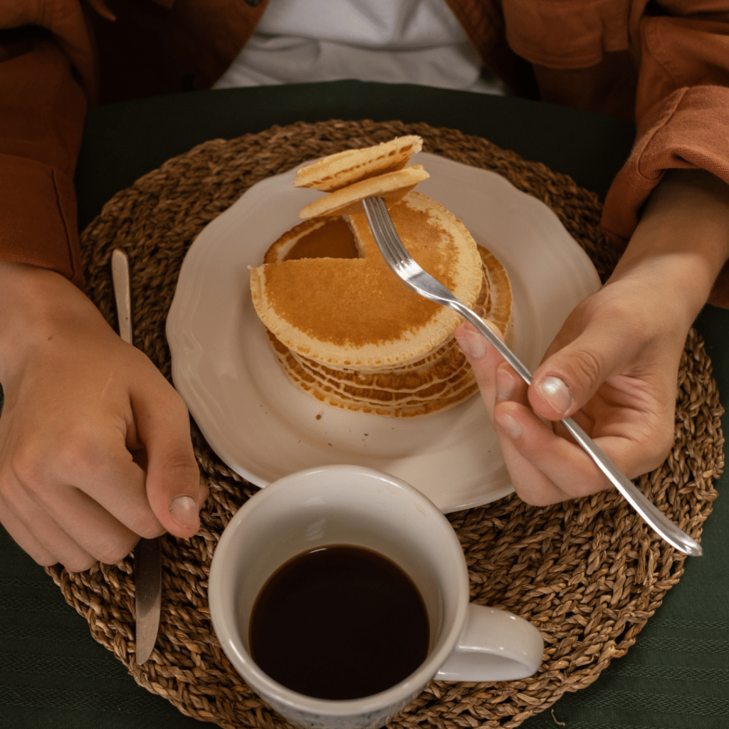homem tomando café da manhã com panquecas e uma xícara de café
