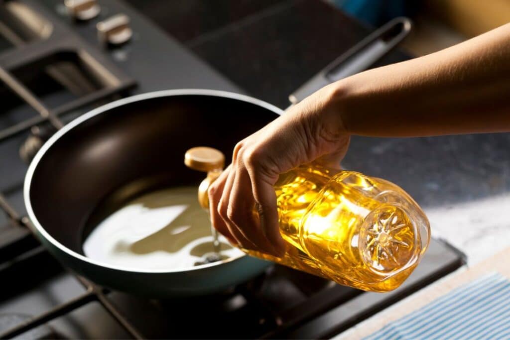 pessoa colocando óleo de girassol em uma panela no fogão